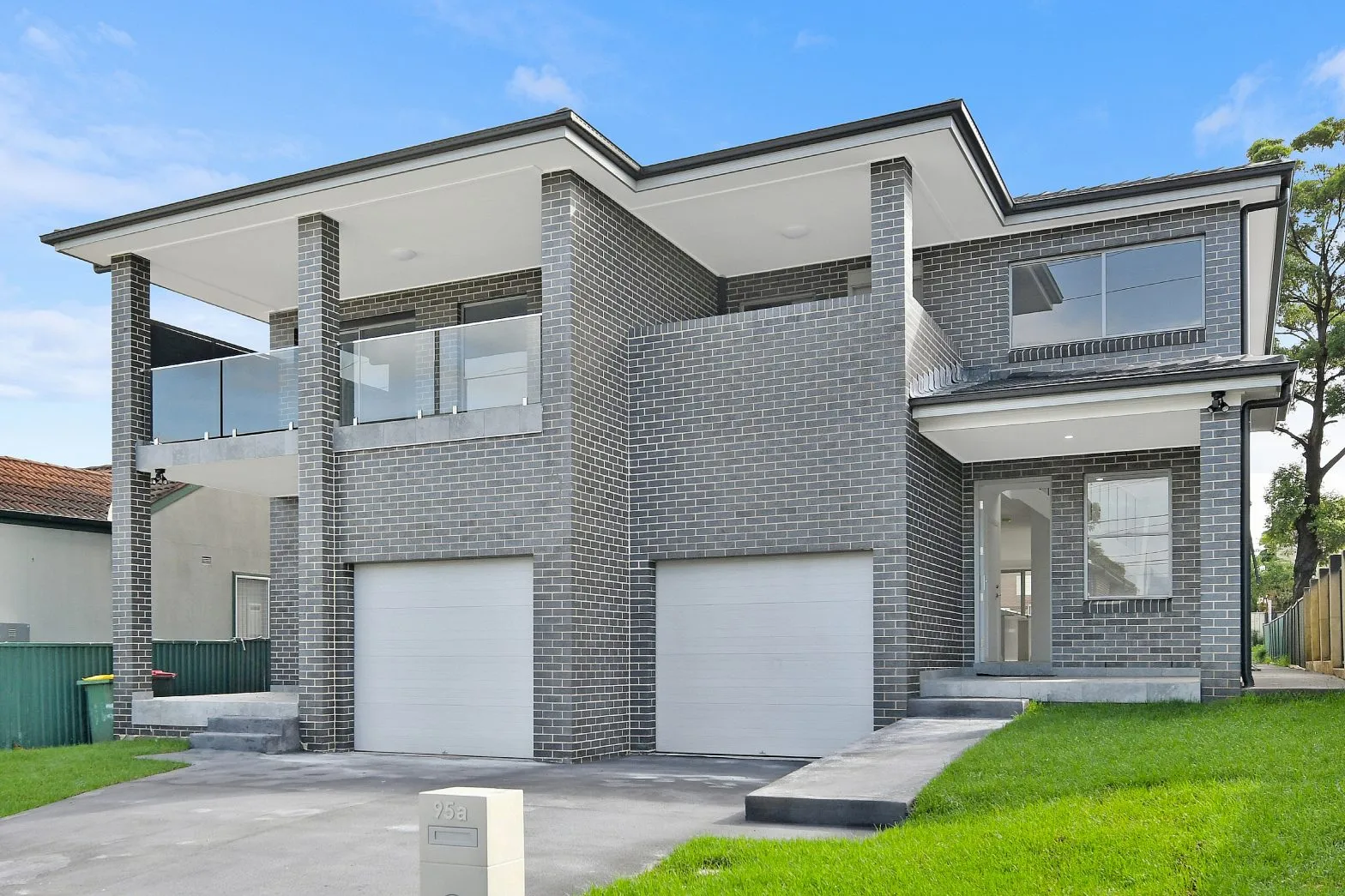 Double-storey brick duplex with two garages, glass balcony, and modern architectural design.